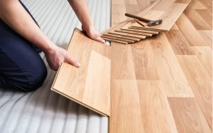 Close-up of a flooring installer laying wood effect flooring planks over a prepared subfloor for a seamless finish.
