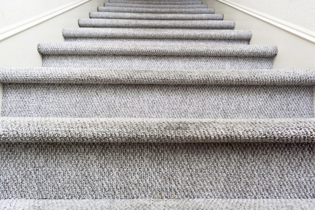 Grey speckled loop pile carpet fitted across full width of staircase treads